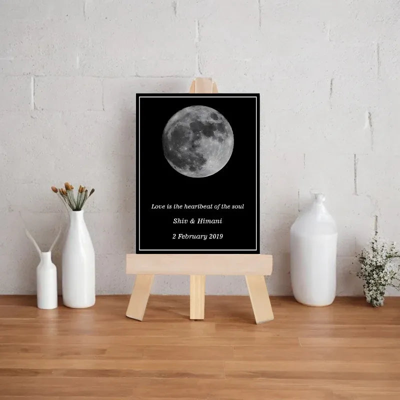 Framed picture of a moon with text on a wooden easel against a white wall.