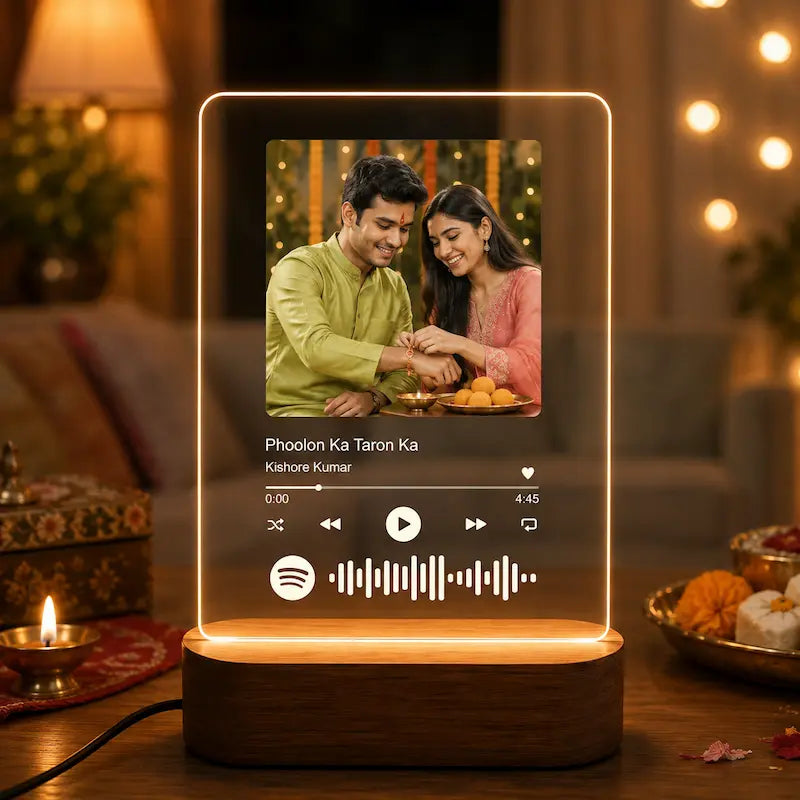 A glowing rectangular LED night light shaped like a music player screen, standing on a wooden base on a table. The screen displays a Spotify-style music interface with the text 'Phoolon Ka Taron Ka' and artist name 'Kishore Kumar', plus a small photo of a couple.