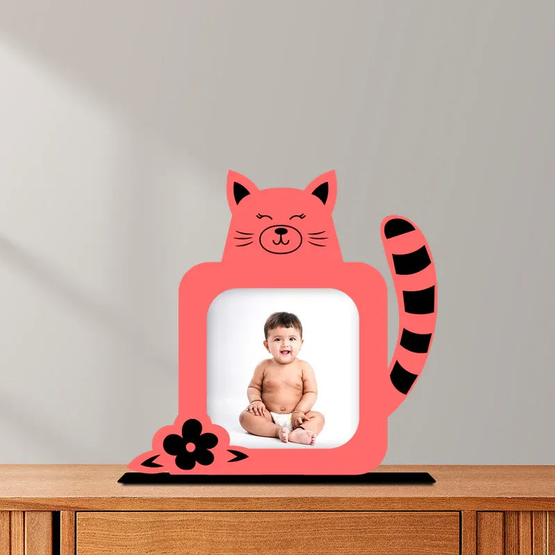 Pink cat-shaped photo frame with a baby photo inside on a wooden surface.