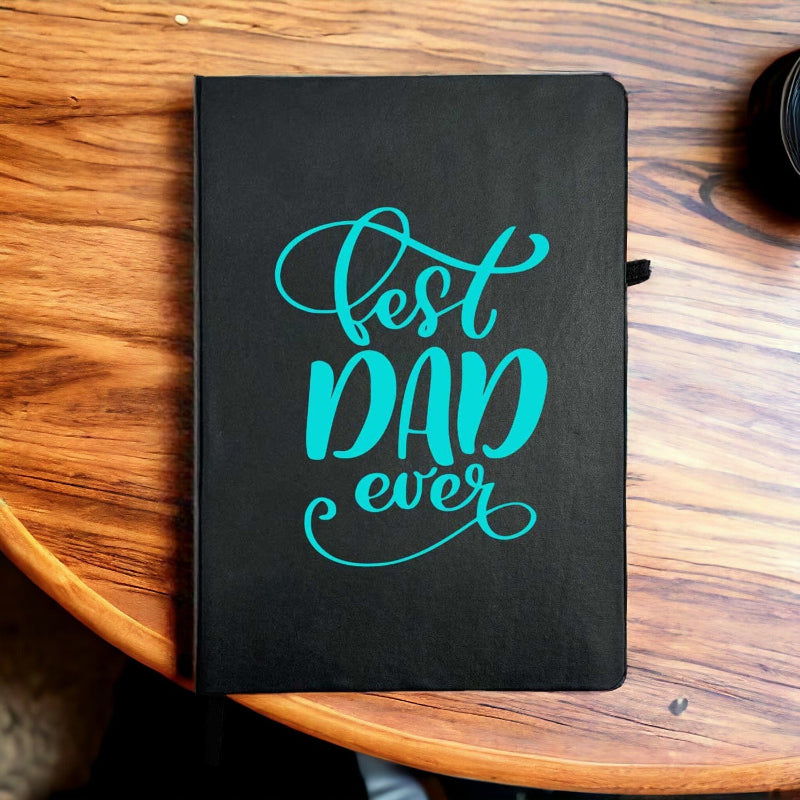 Black notebook with 'Best Dad Ever' in turquoise on a wooden surface