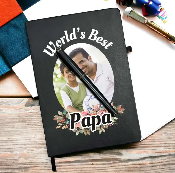 Black notebook with a photo of a father and son and 'World's Best Papa' text on a wooden surface.