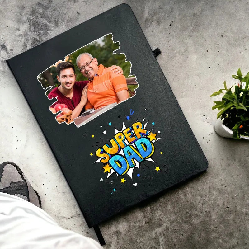 Black notebook with 'Super Dad' design and photo of a man and an older man on a concrete surface.