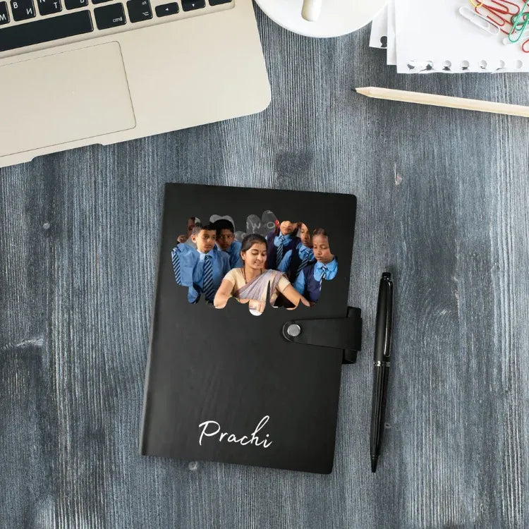 Black notebook with a photo of a woman and children on a wooden desk with a laptop and pen.