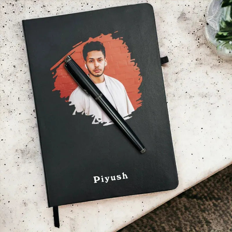 Black notebook with a portrait of a man and the name 'Piyush' on a textured surface.