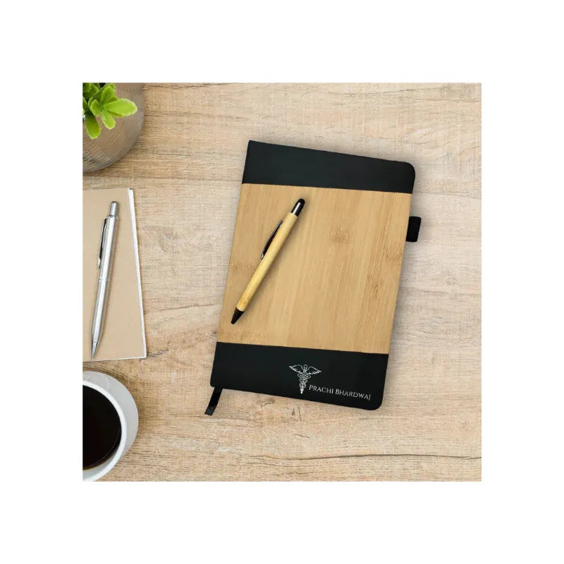 Wooden notebook with black cover on a wooden surface with two pens and a cup of coffee.