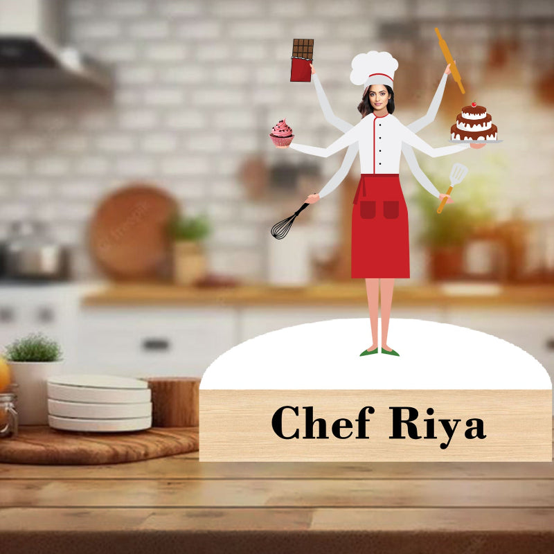 Figurine of a chef with multiple arms holding kitchen utensils and desserts on a wooden base with 'Chef Riya' text, set against a blurred kitchen background.