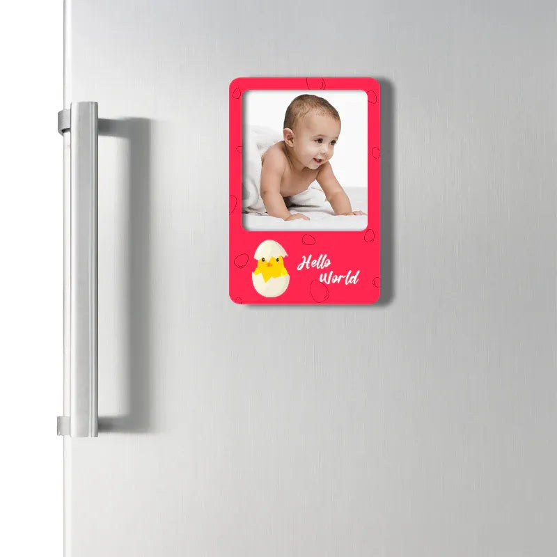 Fridge magnet with a baby photo and 'Hello world' text on a red border, attached to a refrigerator.