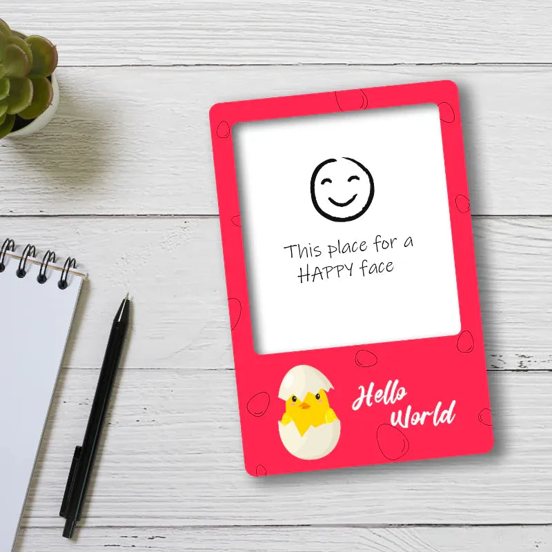 Red photo fridge magnet with a chick illustration and text on a white surface with a pen and plant.