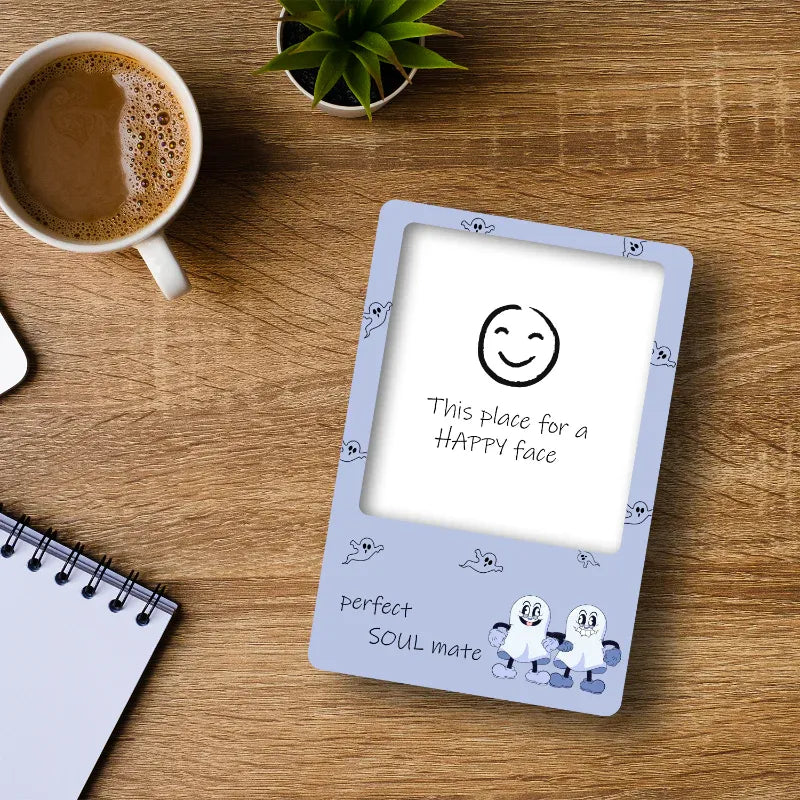Card with smiley face illustration and text on a wooden table with a cup of coffee and plant.