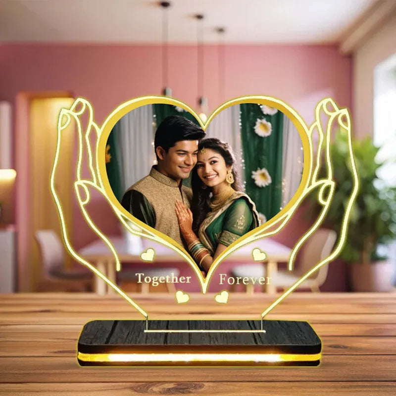 Heart-shaped photo frame with hands holding a couple, placed on a wooden surface.