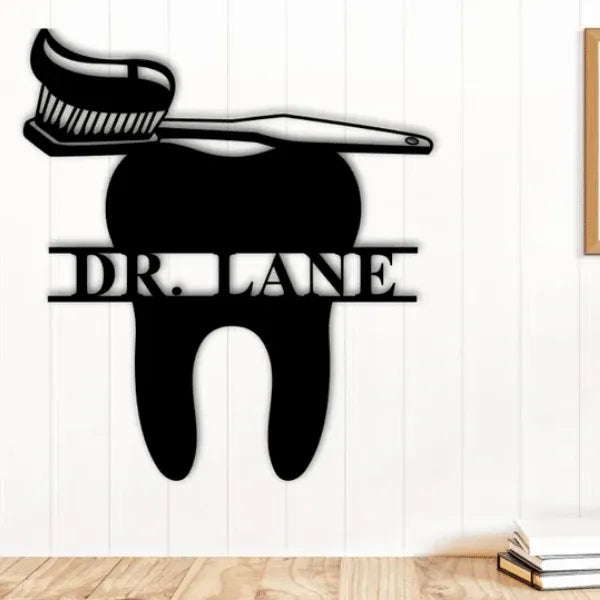 Decorative metal sign shaped like a tooth with a brush on a white wall.