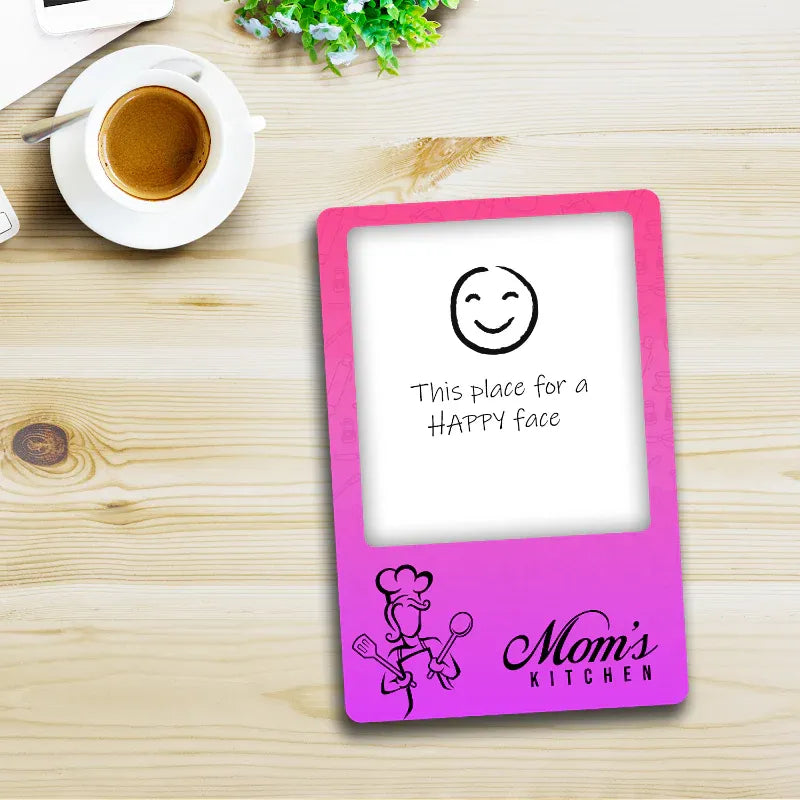 Pink photo frame magnet with 'Mom's Kitchen' design on a wooden table with a cup of coffee.