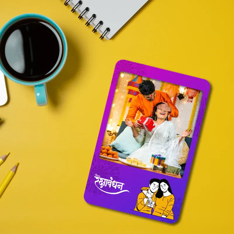 Card with a rakhi on a purple border on a yellow background with a cup of coffee and notebook.