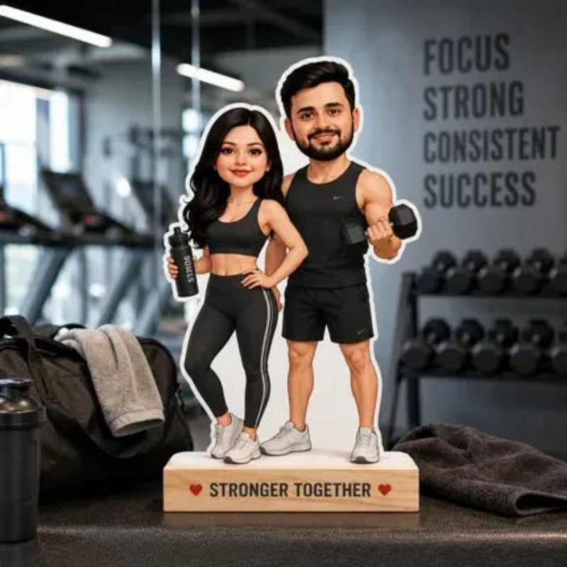 A custom die-cut cardboard cutout of a couple in workout attire, standing on a wooden base engraved with 'STRONGER TOGETHER'. The cutout features a cartoon-style design of a man and woman in black athletic wear, standing in a gym setting with dumbbells and a towel nearby.