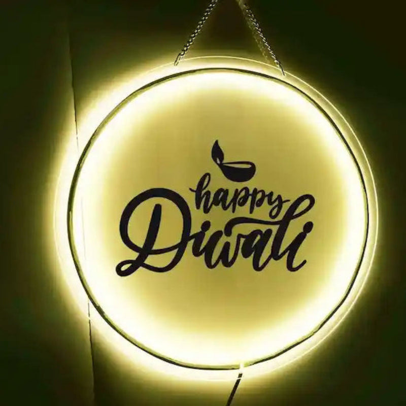 A glowing, round, happy Diwali neon ring light sign hanging against a dark background, featuring the text 'Happy Diwali' in black script, with a small diya illustration above it.
