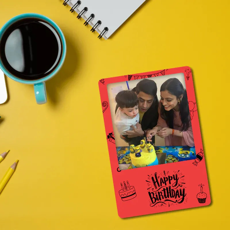 Red 'Happy Birthday' fridge magnet with a family photo on a yellow background with a cup of coffee and pencils.