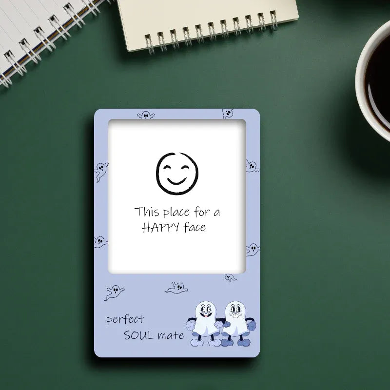 Decorative frame with a smiley face design on a green surface with a notebook and coffee cup.