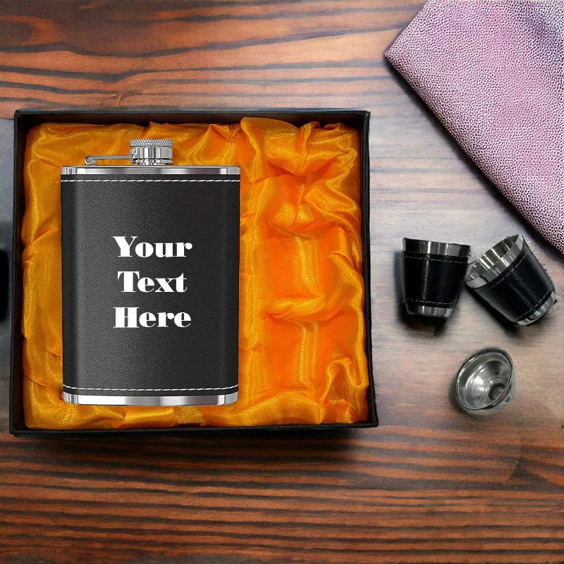 Black flask with 'Your Text Here' text in a box on a wooden surface with shot glasses.
