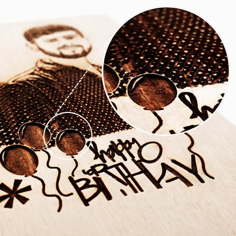 Close-up of a personalized wooden birthday card or plaque with a laser-engraved portrait, balloons, and the words “happy birthday,” shown with a circular magnified inset of the wood grain and burn pattern.
