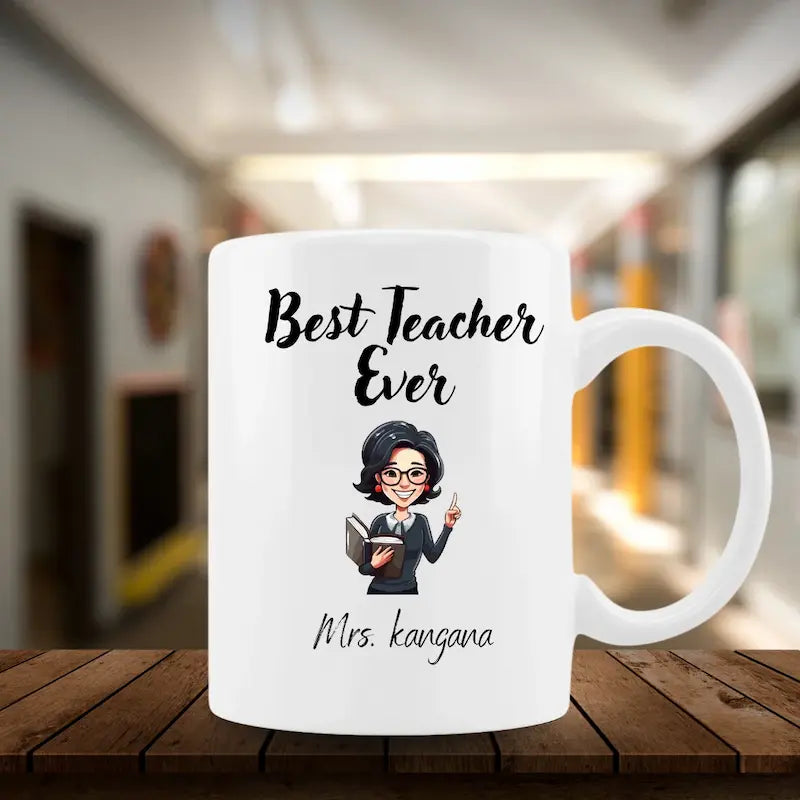 A white ceramic mug with a cartoon illustration of a female teacher and the text 'Best Teacher Ever' and 'Mrs. kangana', displayed on a wooden table with a blurred school hallway background.