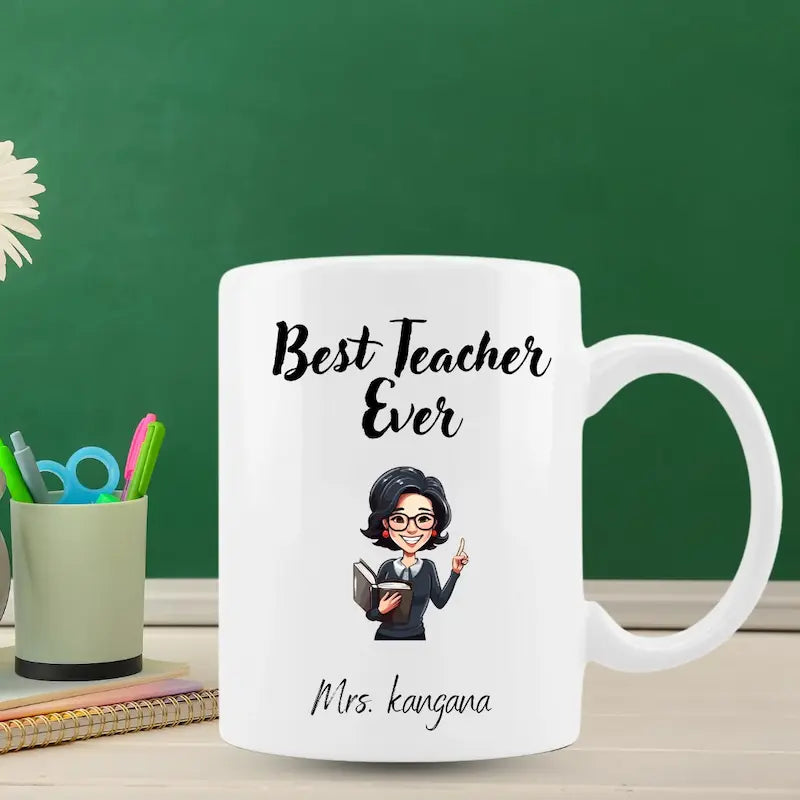 A white ceramic teacher mug with a cartoon illustration of a female teacher and the text 'Best Teacher Ever' and 'Mrs. Kangana ', placed on a desk in front of a green chalkboard background.