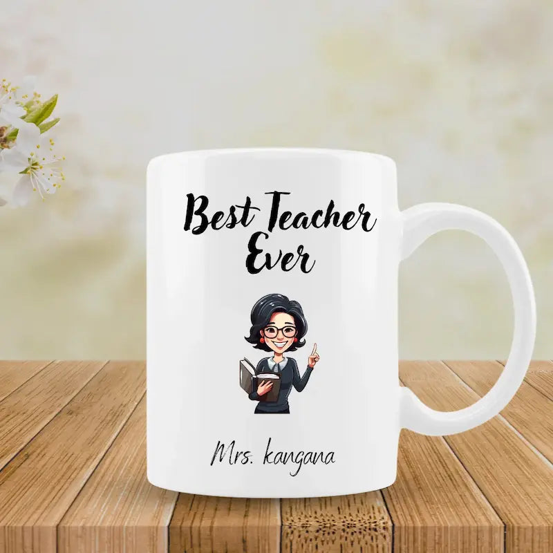 A white ceramic mug with a cartoon illustration of a female teacher and the text 'Best Teacher Ever' and 'Mrs. kangana', displayed on a wooden surface with a soft, blurred background.