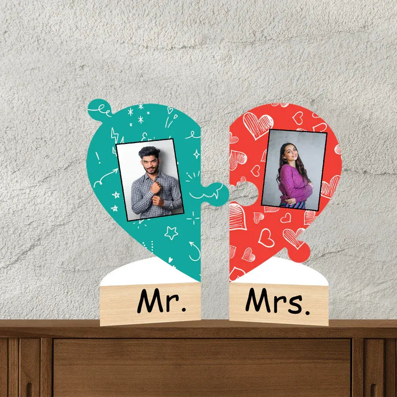 Two heart-shaped photo frames labeled 'Mr.' and 'Mrs.' on a wooden surface with a light gray wall background.