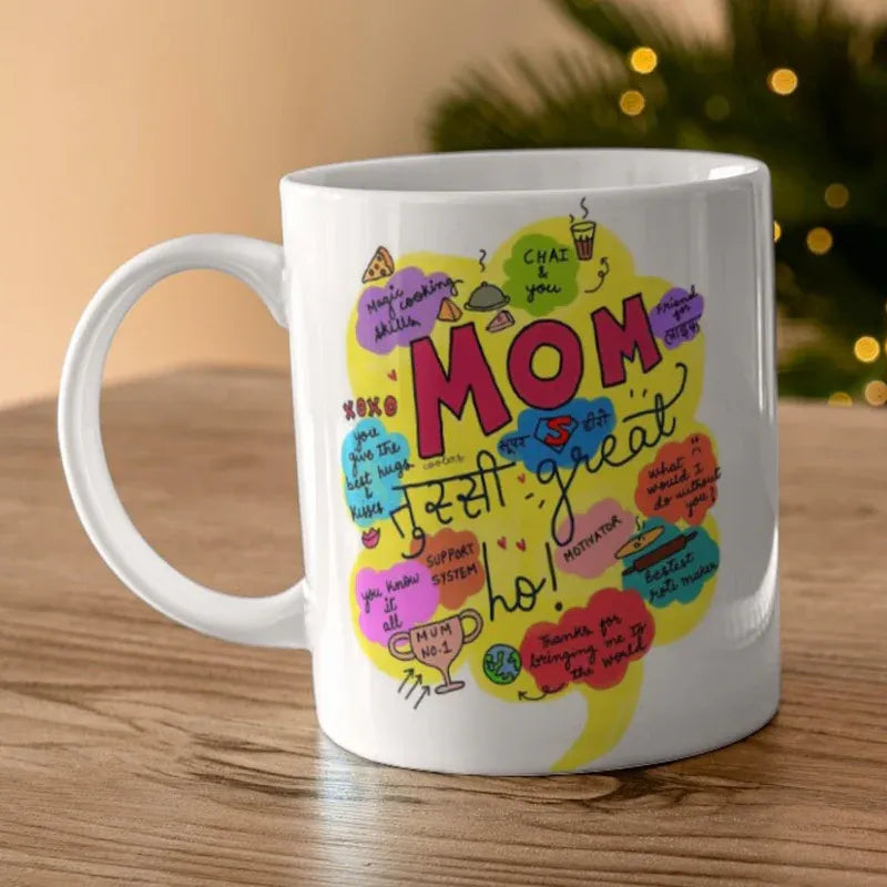 White mug with colorful 'Mom is just so great' design on a wooden surface.