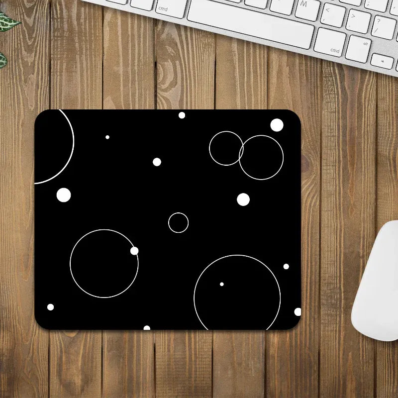 Black mouse pad with white circular designs on a wooden desk with a keyboard and mouse.