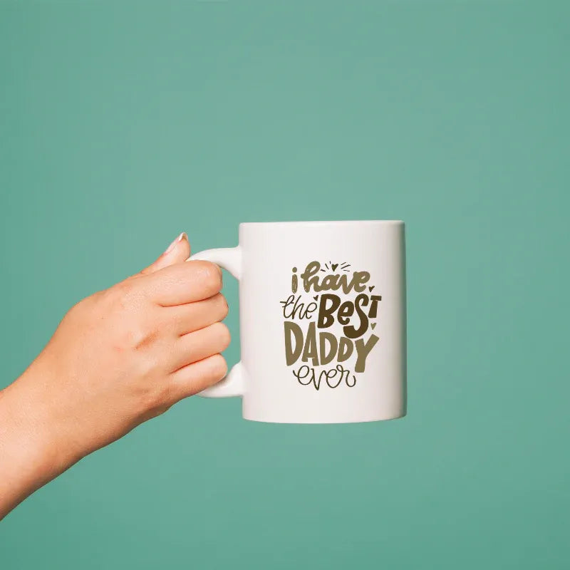 Hand holding a mug with 'I have the best daddy ever' text on a teal background