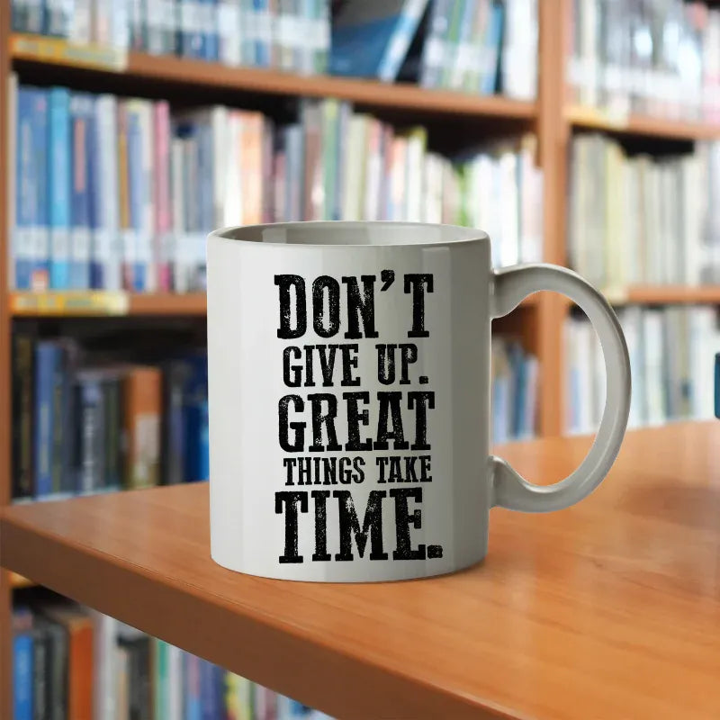 Mug with 'Don't give up. Great things take time.' text on a wooden table with a bookshelf background