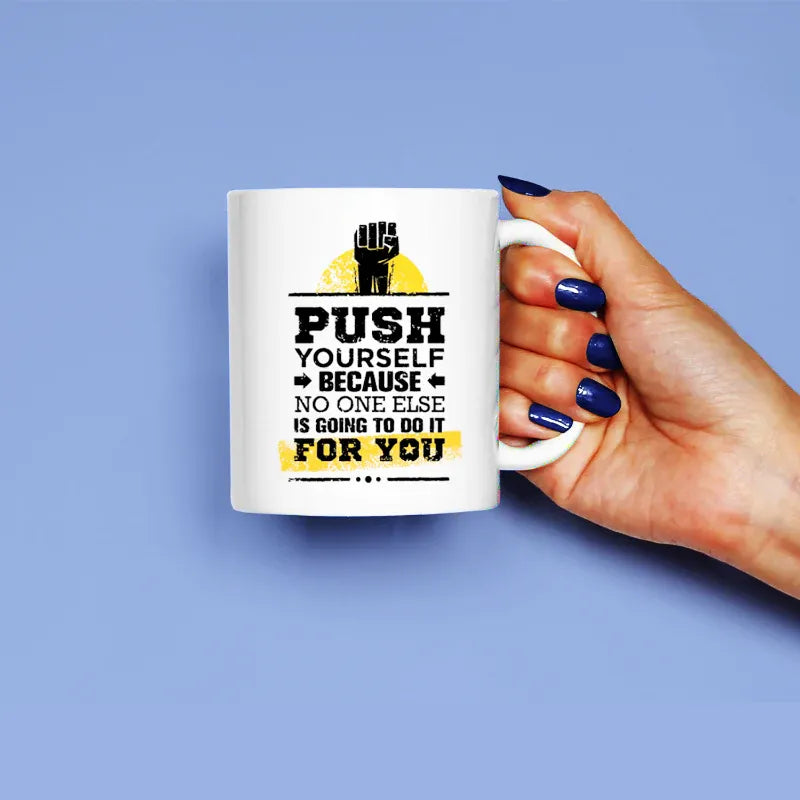 A hand holding a white ceramic mug with a motivational quote printed on it.