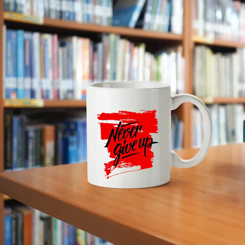 White mug with 'Never Give Up' text on a wooden table in front of bookshelves
