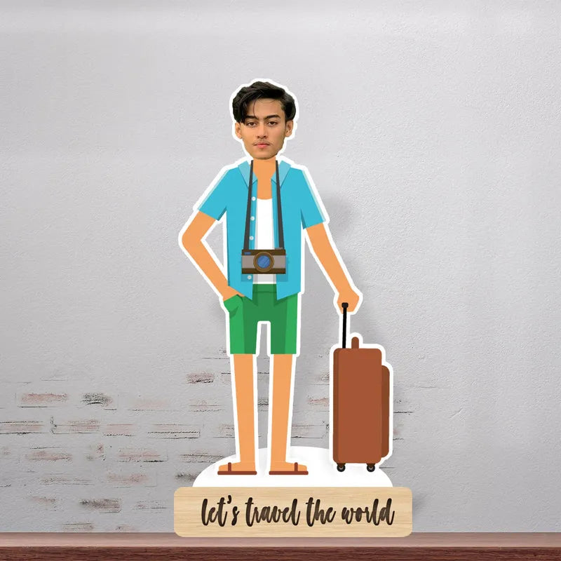 Cardboard cutout of a person in travel attire with a suitcase and camera, on a wooden stand with 'Let's travel the world' text.