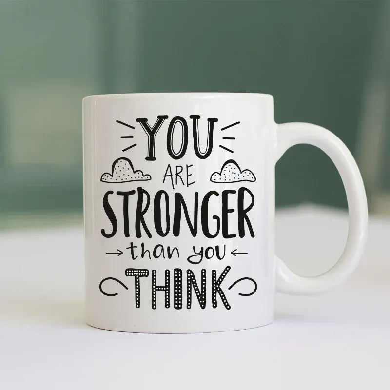 White mug with motivational quote 'You are stronger than you think' on a blurred background