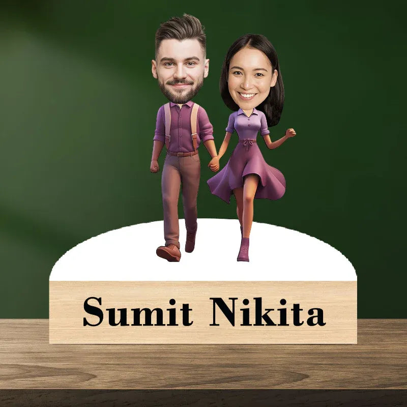 Bobblehead figures of a man and woman holding hands with a wooden base displaying 'Sumit Nikita' on a green background.