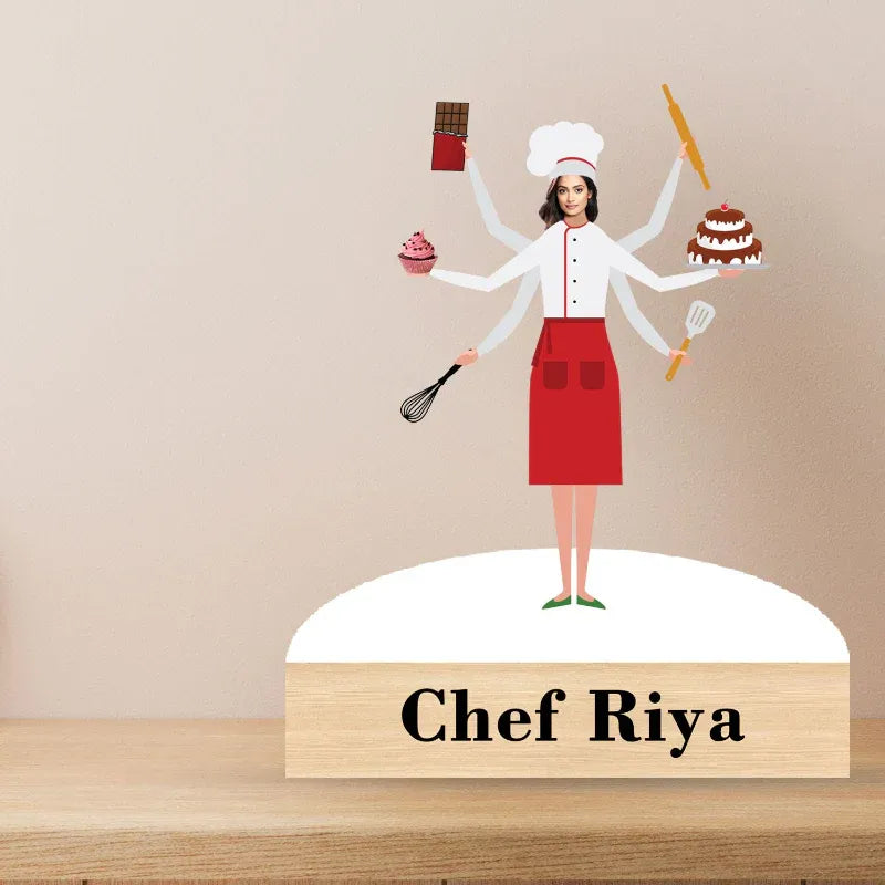 Cake topper with a stylized chef character holding various cooking utensils and desserts, with 'Chef Riya' on a base.