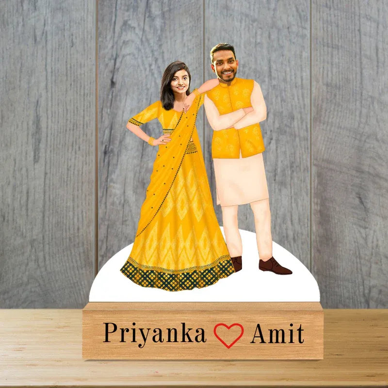 caricature of a man and woman in traditional attire with a wooden base displaying 'Priyanka ❤️ Amit' on a wooden base