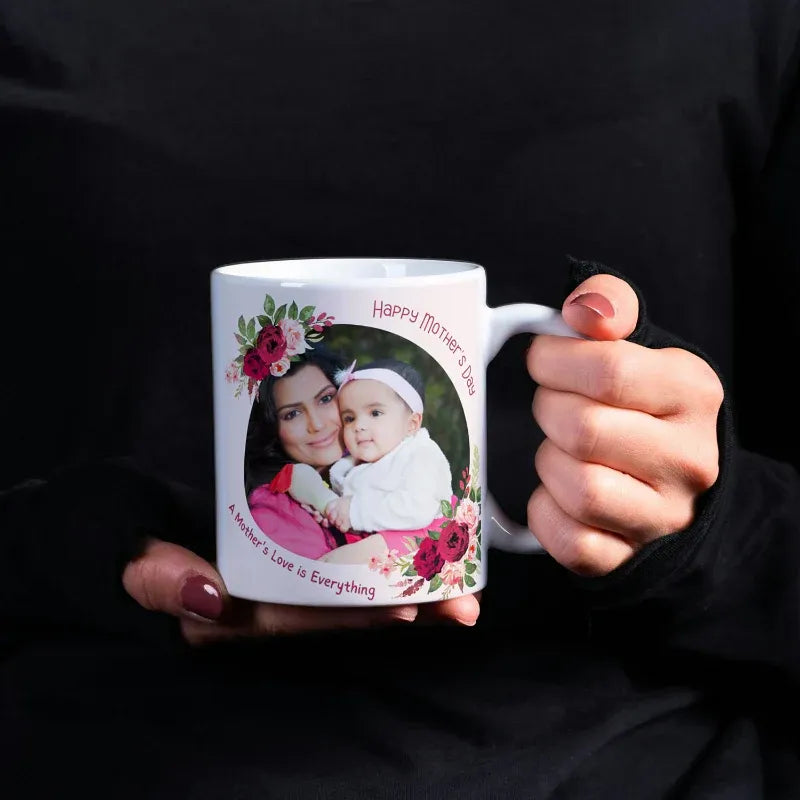 Person holding a mug with a photo of a woman and child and floral design, text 'Happy Mother's Day'.