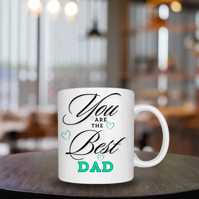 White mug with 'You are the best dad' text on a wooden table in a blurred cafe setting
