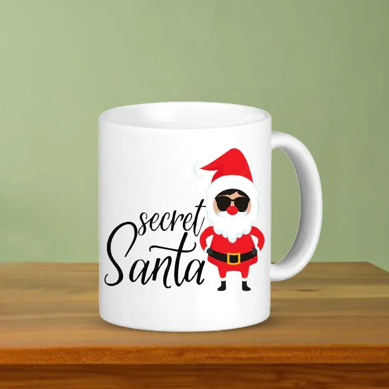 White mug with a cartoon Santa Claus design and 'secret Santa' text on a wooden surface.