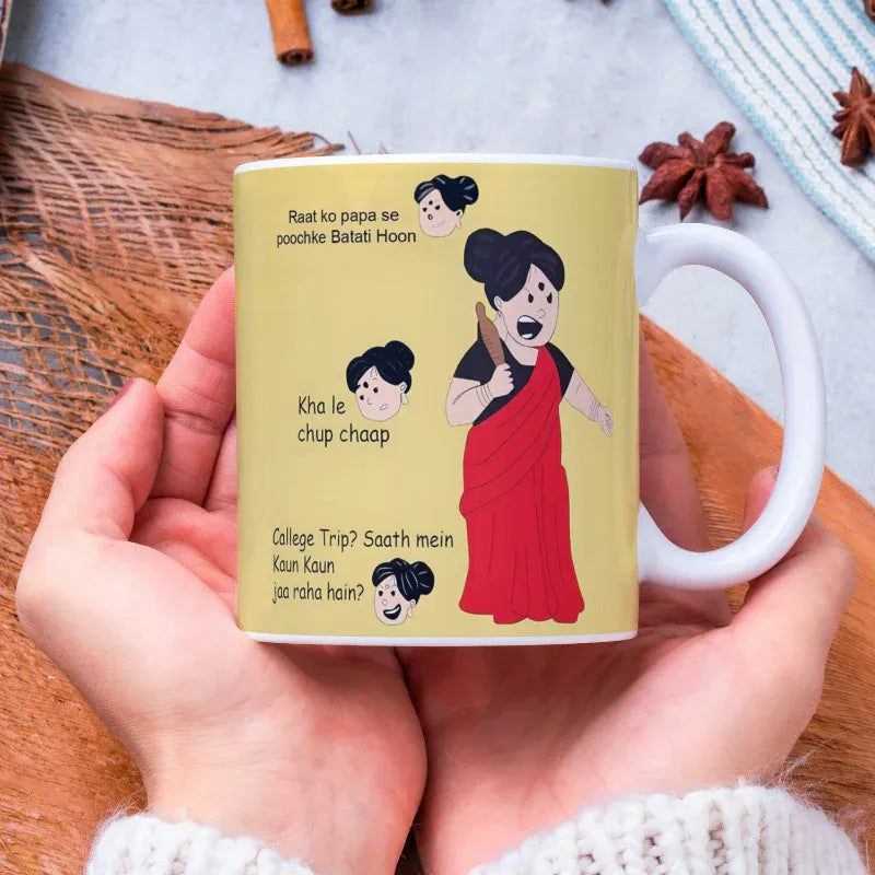 Mug with cartoon characters and text held by a hand on a wooden surface.