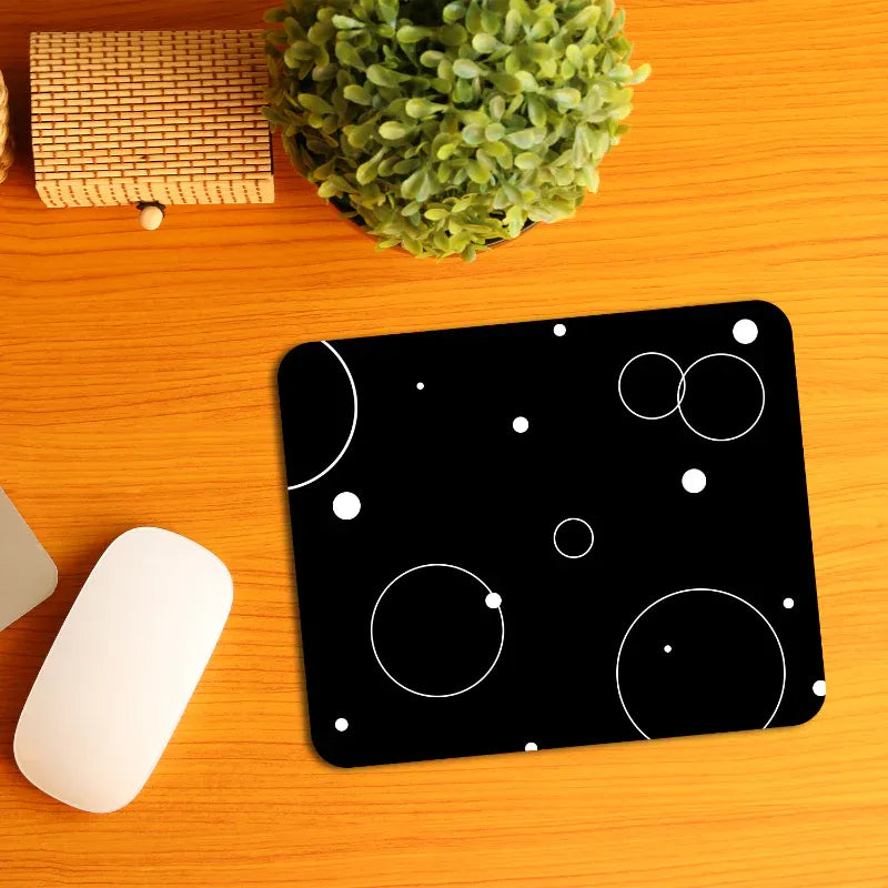Black mouse pad with white circular designs on a wooden desk with a plant and mouse.