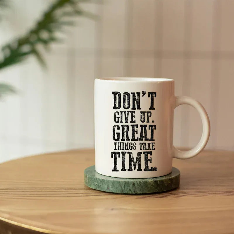 Mug with 'Don't give up. Great things take time.' text on a wooden table with a plant in the background