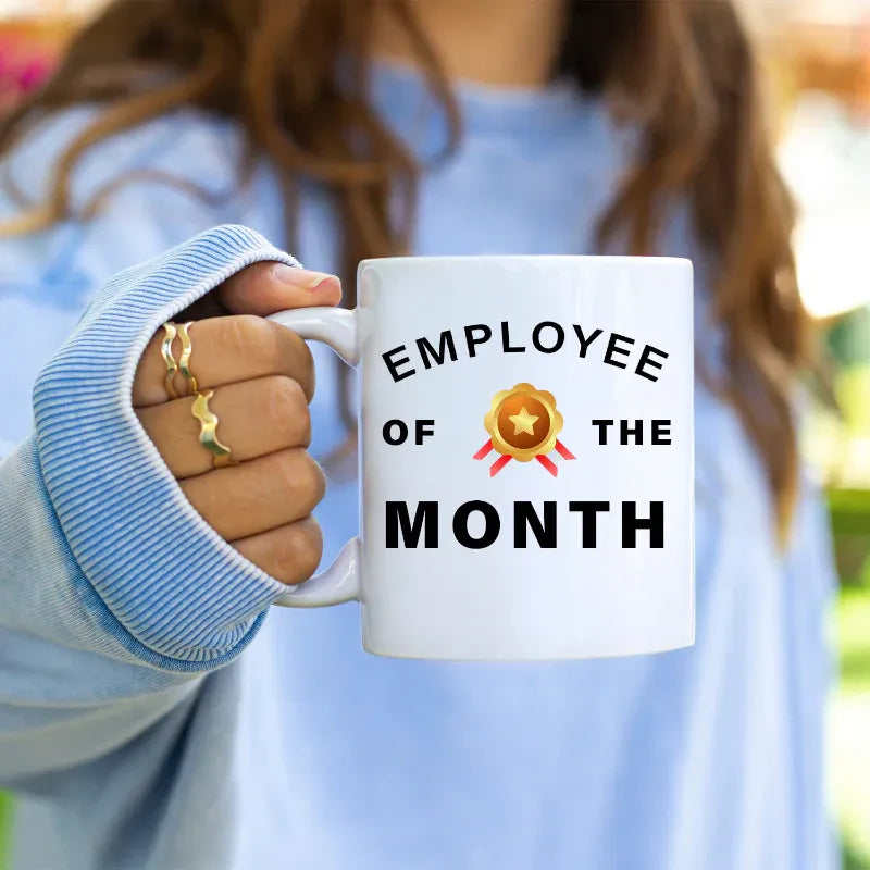 Person holding a white mug with 'Employee of the Month' text