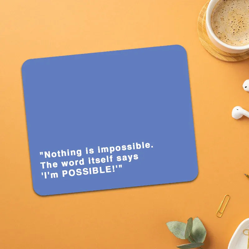 Blue mouse pad with motivational quote on an orange surface with a cup of coffee and earbuds.