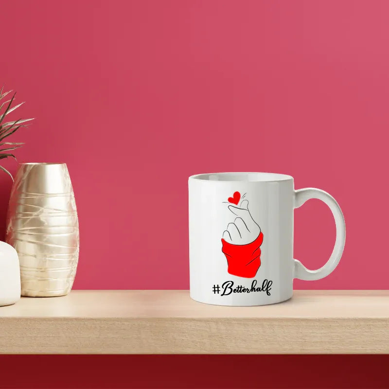 White mug with '#Betterhalf' design on a wooden surface with a pink background