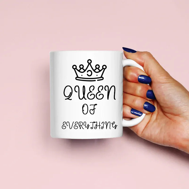 Hand holding a mug with 'Queen of Everything' text on a pink background