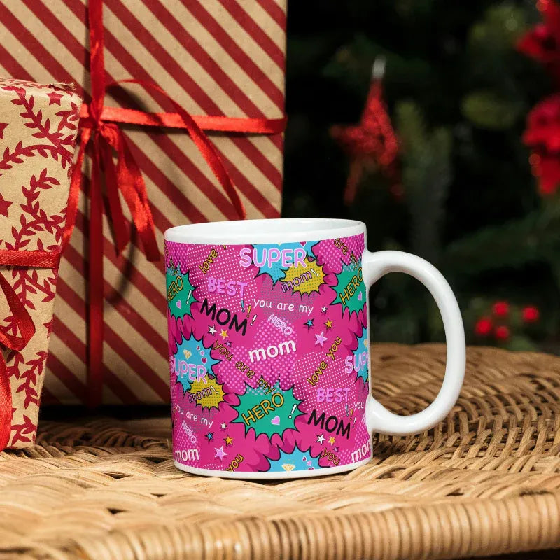 Pink mug with 'Super Best Mom' text in a festive setting with wrapped gifts and red ribbons.
