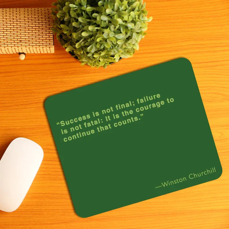 Green mouse pad with Winston Churchill quote on a wooden desk with a plant and mouse.